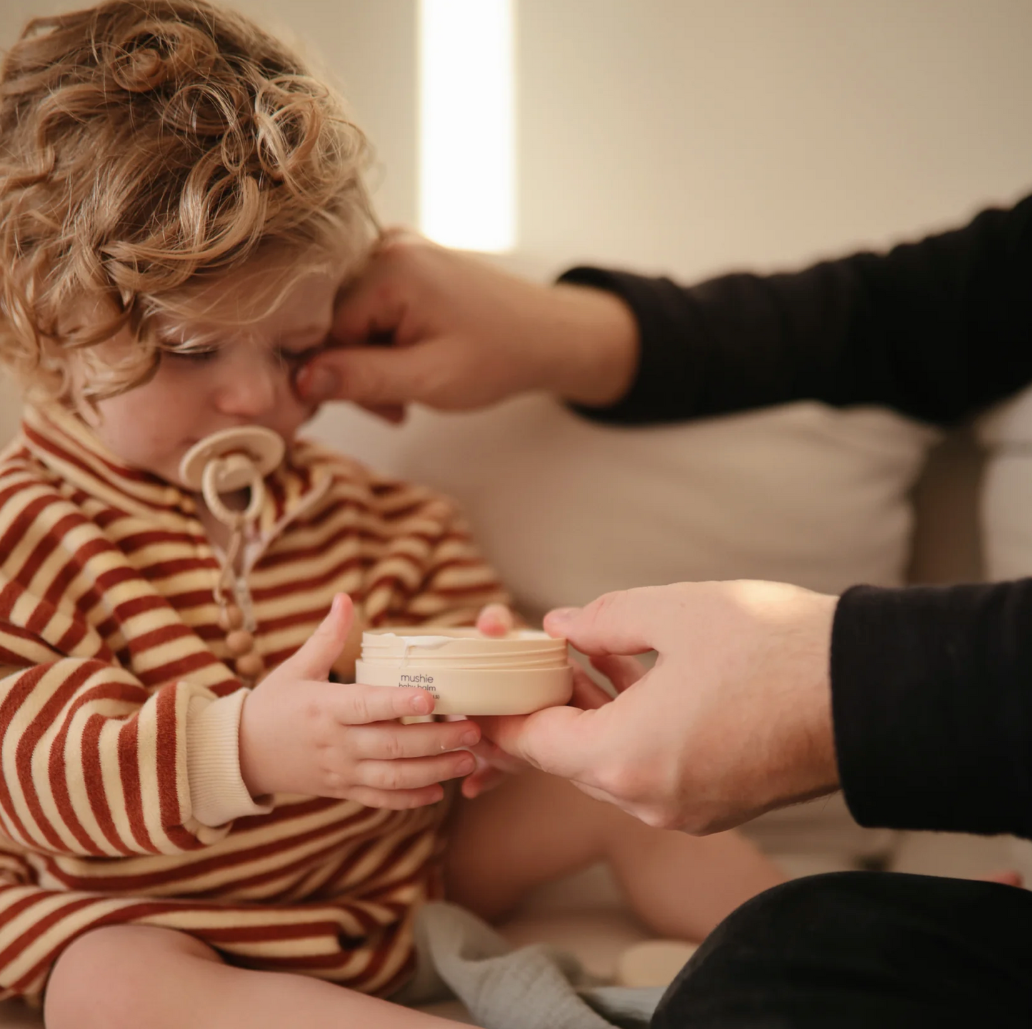 Baby balm fragrance free from Mushie, toddler holding open product