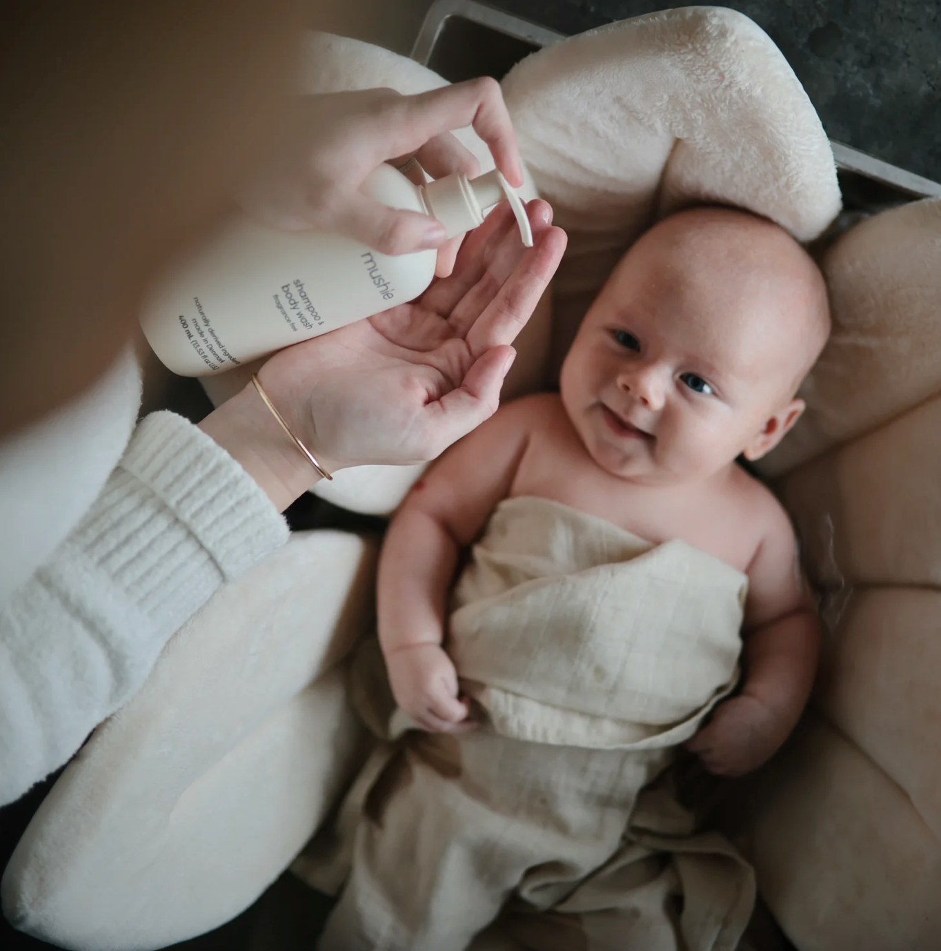 shampoo & body wash from Mushie, mother holding bottle and baby in a crib