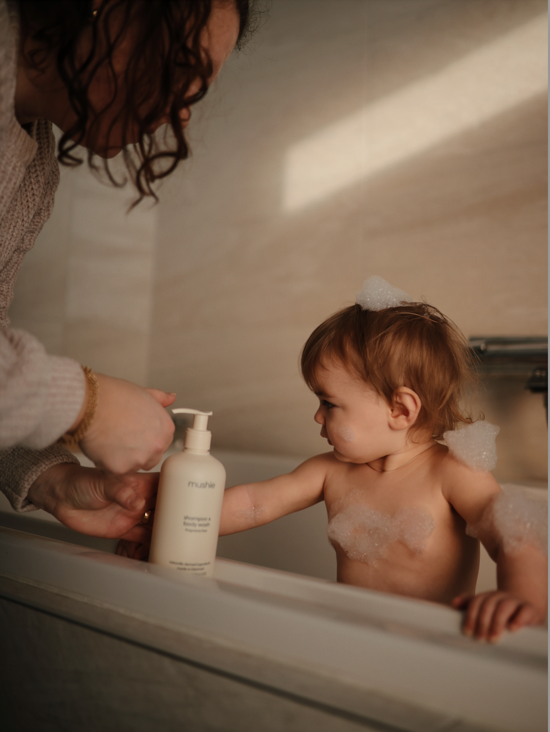 shampoo & body wash, fragrance free, from Mushie. Baby in bathtub with mother.