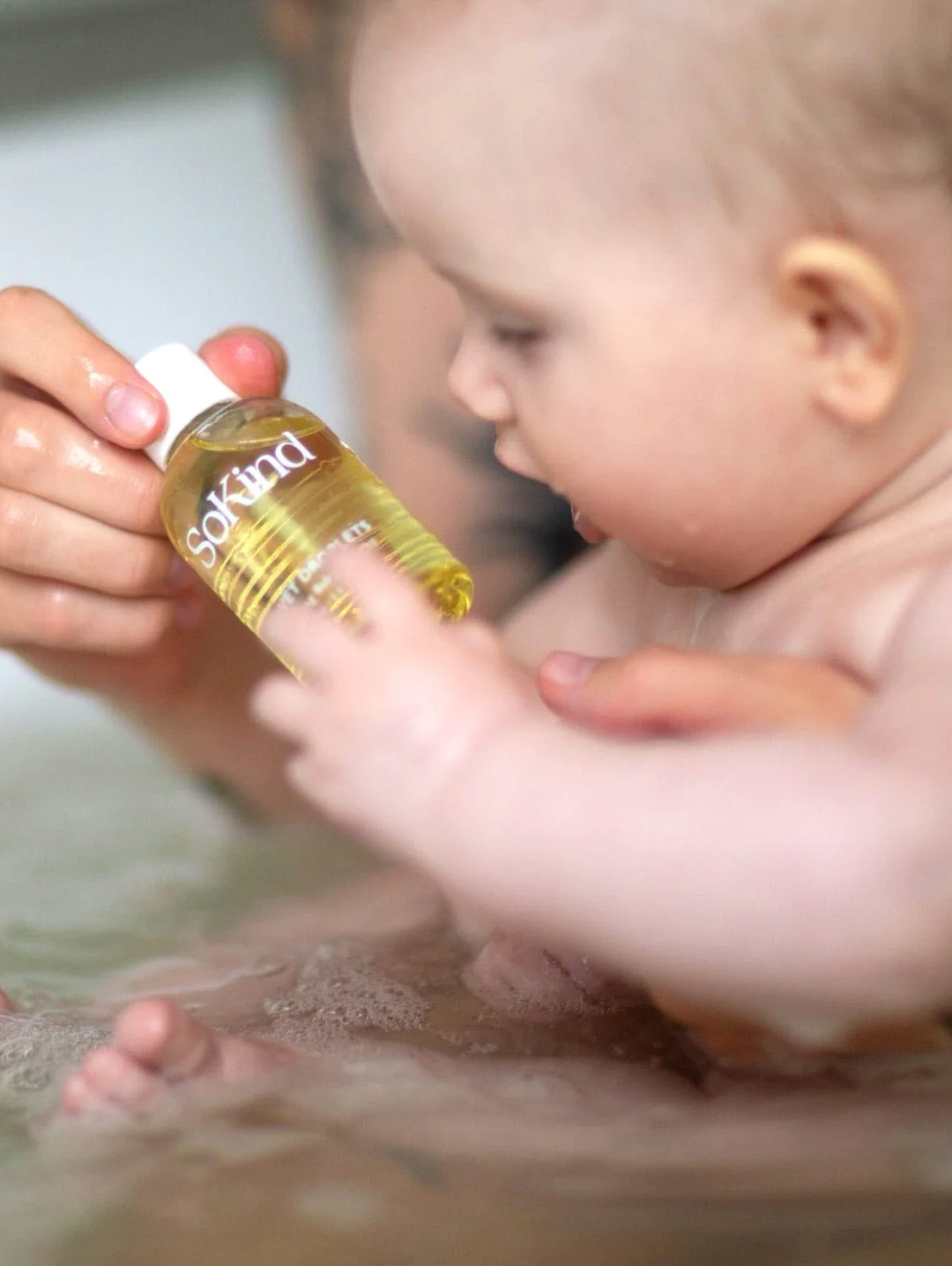 Velvet Droplets from SoKind, a nurturing baby bath oil, baby playing with it in the bath